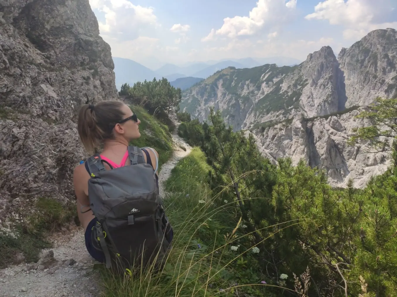 Turistka s batohem sedí na horské stezce a dívá se na skalnaté hřebeny